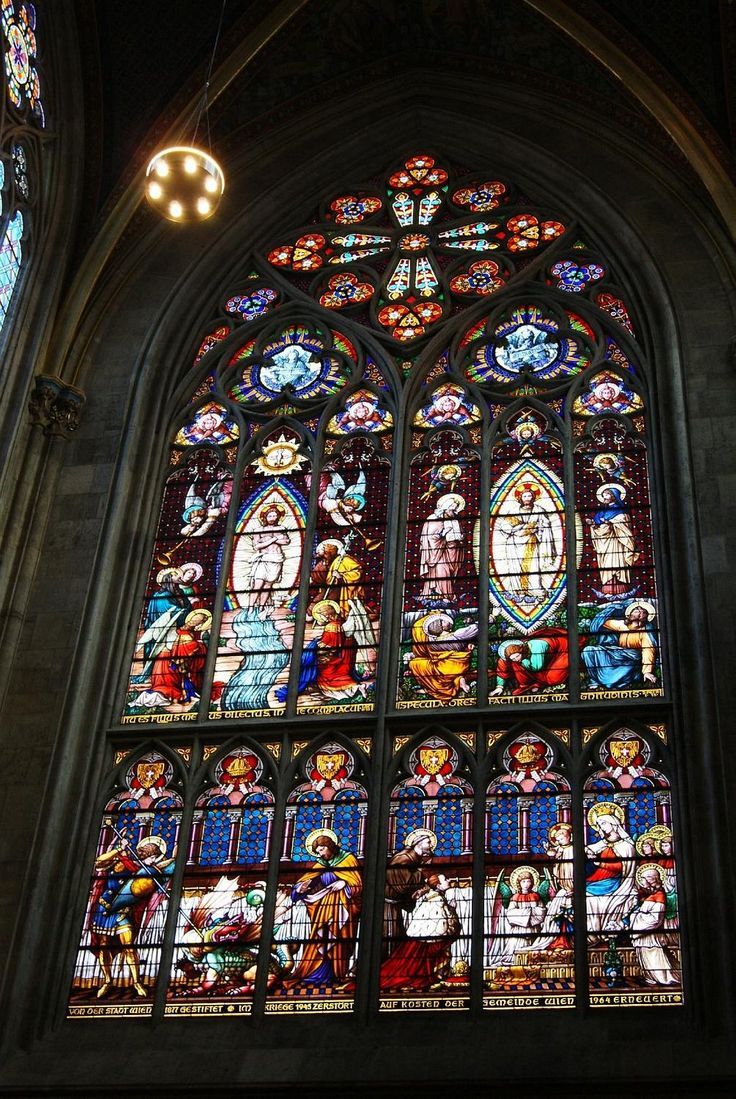 The stained glass window 'Verklärung Christi' in the Votive Church in Vienna, Austria, depicts the Luminous Mystery of the Transfiguration, where Jesus is radiantly transfigured in divine light before the apostles Peter, James, and John, with the figures of Moses and Elijah appearing beside him